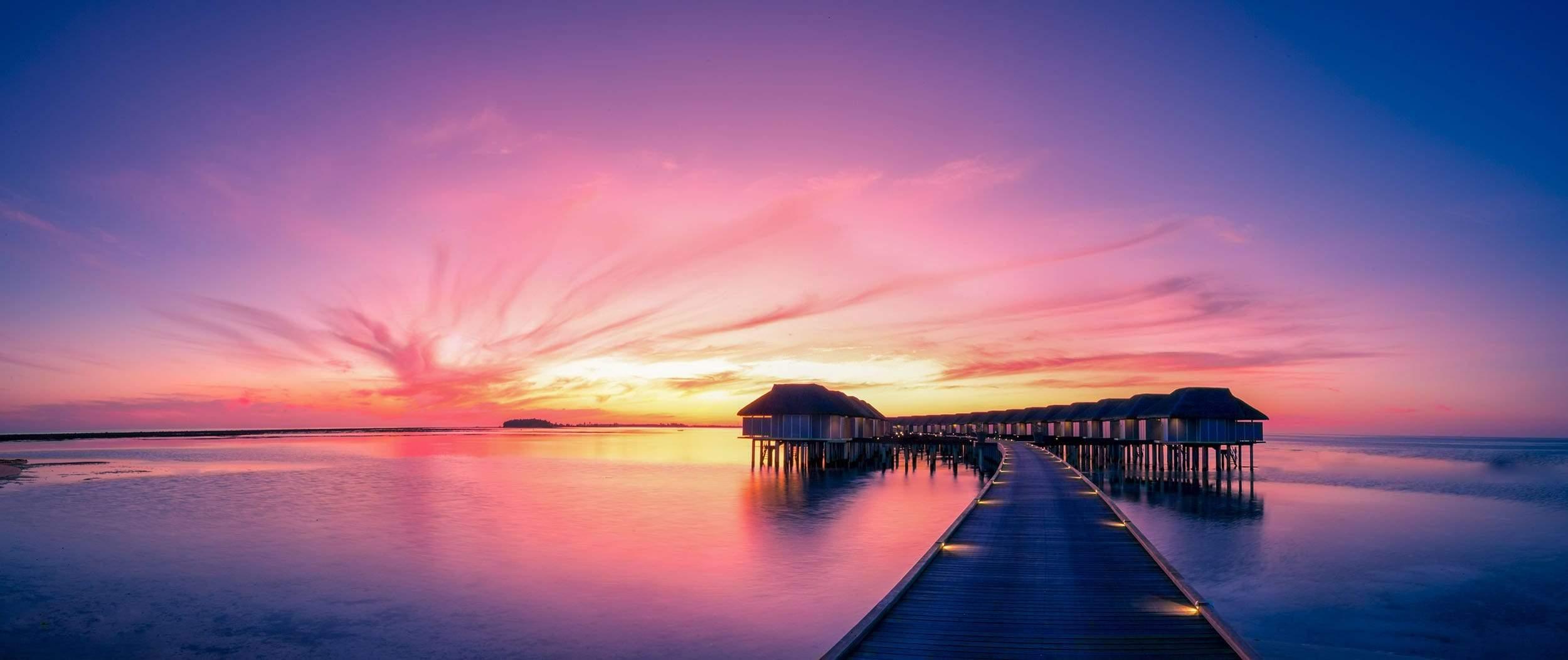 Sunset on Maldives island water villas resort along wooden pier
