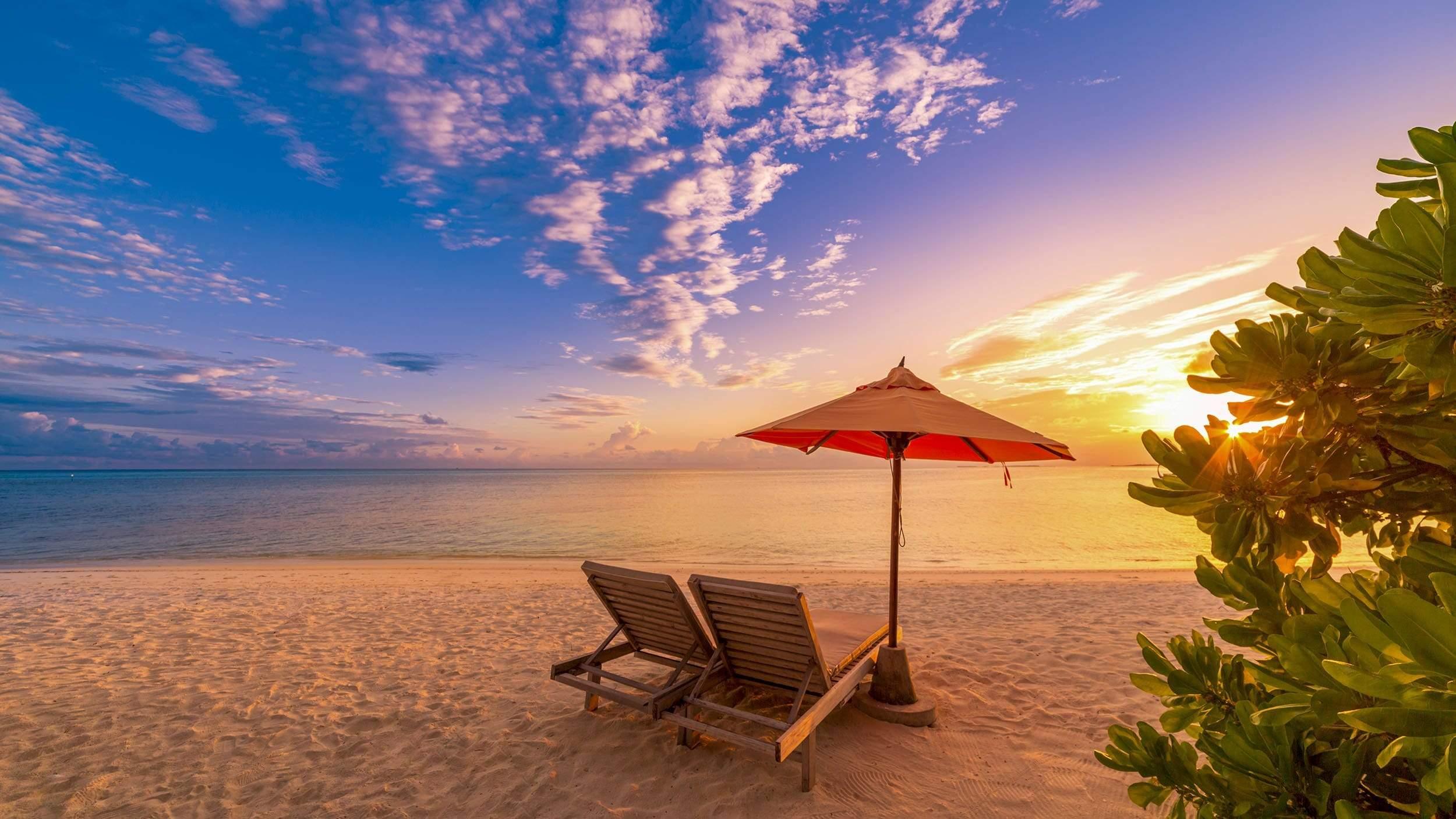 Two chairs under umbrella on sandy beach sunset