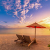 Two chairs under umbrella on sandy beach sunset